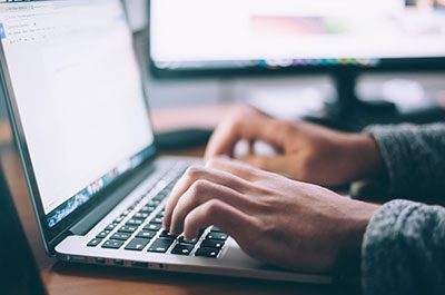 A close up photo of hands typing on the keyboard of a laptop computer